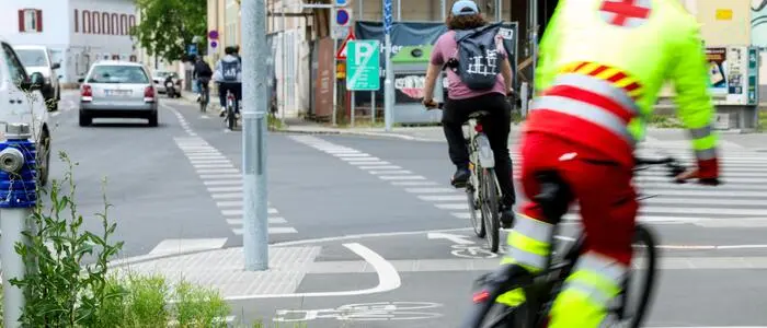 Fahrradfahrer radeln auf einem Fahrradstreifen neben der Straße. Einer trägt eine Rettungsuniform