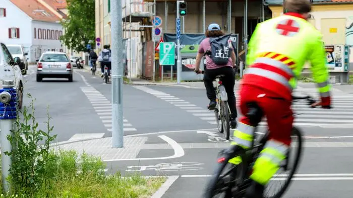 Fahrradfahrer radeln auf einem Fahrradstreifen neben der Straße. Einer trägt eine Rettungsuniform
