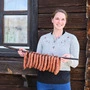 Eine Frau hält einen Spieß voller geräucherter Fleischwaren in den Händen und lächelt in die Kamera.