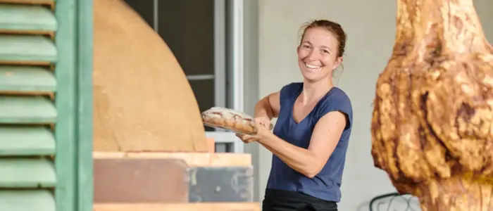 Eine Frau mit einem Laib Brot in der Hand lacht in die Kamera