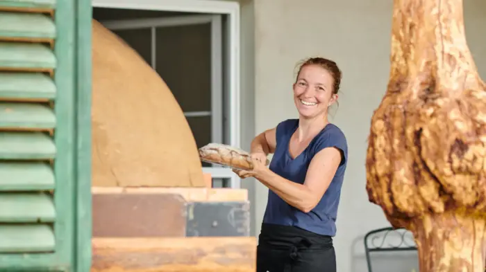 Eine Frau mit einem Laib Brot in der Hand lacht in die Kamera