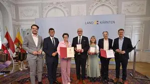  Mehrere Personen stehen in einem Saal und halten Urkunden in die Kamera