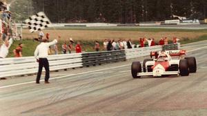 Siegfried Mandl beim Abwinken des Rennens im Jahr 1984, bei welchem Niki Lauda gewonnen hatte. Die hellen Punkte hinten auf den Bäumen sind Zuschauer