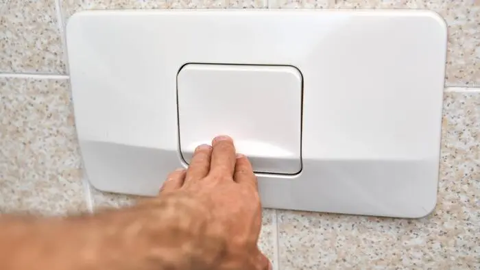 Eine Hand betätigt die Toilettenspülung in einem Badezimmer