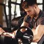 Handsome man doing biceps lifting barbell on bench in a gym