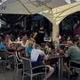 Blick in einen gut gefüllten Gastgarten, ein Kellner räumt gerade einen Tisch ab