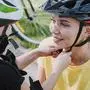 Little girl helping mother to put on bicycle helmet