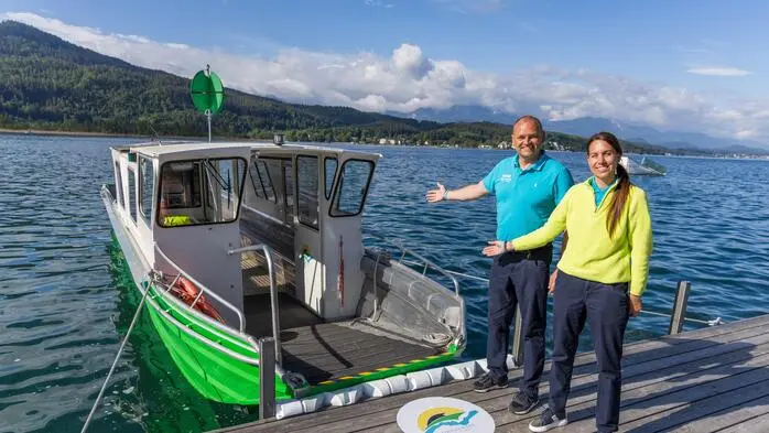 Eine Frau und ein Mann stehen auf einem Steg am Wörthersee und deuten auf eine Fähre