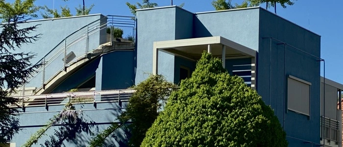 Der Lärm der Grabenstraße ist kaum zu hören. Glyzinien ranken sich an eigens hierfür angebrachten Stangen die blaue Fassade hinauf und auf dem Flachdach breiten Ginkobäume ihre noch jungen Kronen aus.