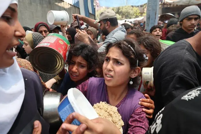 Palestinians gather for a hot meal at a food distribution point in the Nuseirat camp for refugees in the central Gaza Strip on May 21, 2025. Gazans waited desperately for vital supplies on May 21 after Israel said it let in dozens of UN trucks but faced mounting international pressure to increase the aid flow and abandon its intensified military campaign. (Photo by Eyad BABA / AFP)