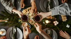 Top view close up of friends clinking glasses while enjoying Christmas dinner together sitting by elegant dining table with candles