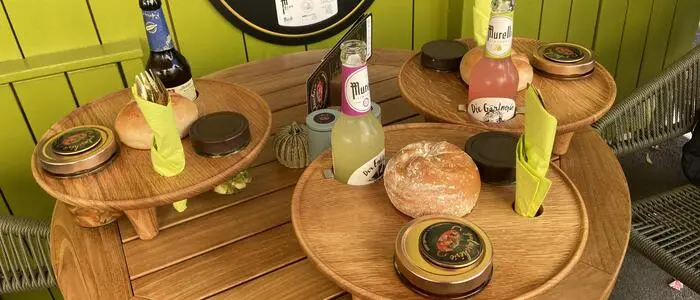 Originelle Idee: Serviert wird das Gulasch im Glas auf einer Holzplatte, die auch Öffnungen für ein Glas Spätzle, Besteck und eine 0,3-Liter-Flasche beinhaltet, in der Mitte ist Platz für eine runde Semmel.