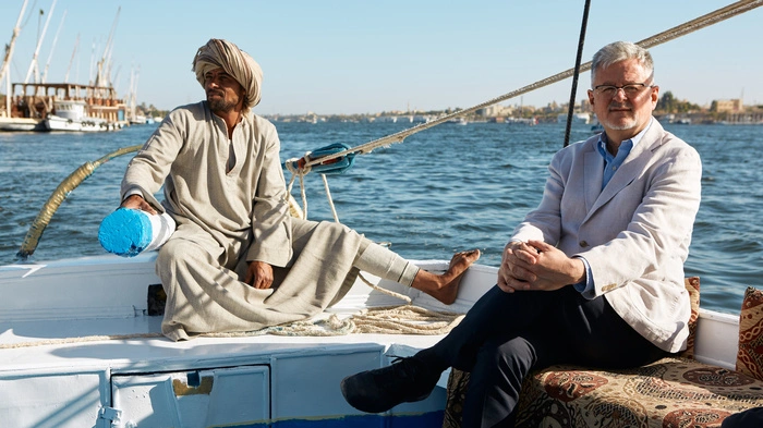 Moderator Christopher Clark sitzt ganz gemütlich auf einem Boot auf dem Nil in Ägypten, neben ihm der Steuermann.
