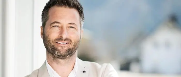 Ein Mann in einem beigen Anzug lehnt lässig gegen eine Wand