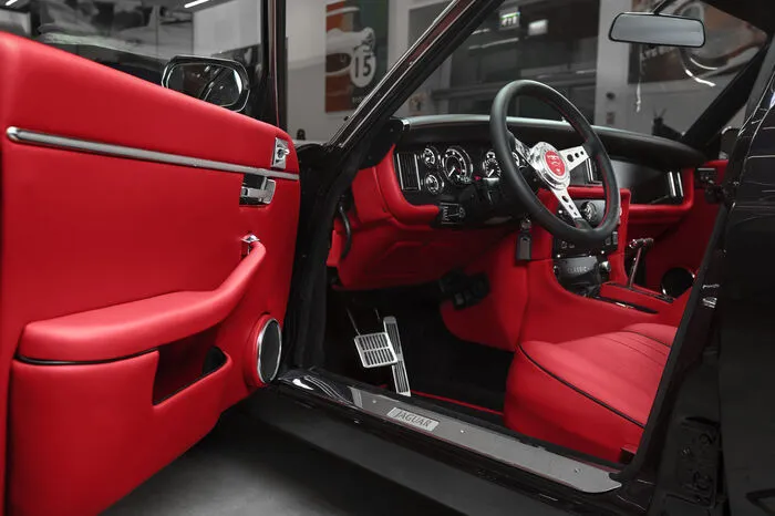 Im Interieur des „Greatest Hits“-Modells trifft klassischer Jaguar Stil auf moderne Komfort- und Infotainment-Funktionen. Die von Hand bezogenen, roten Ledersitze tragen schwarze Keder. In dieser Farbe sind auch die Teppiche und der Dachhimmel gehalten.