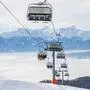Ein Sessellift über einer Skipiste, im Hintergrund Bergpanorama