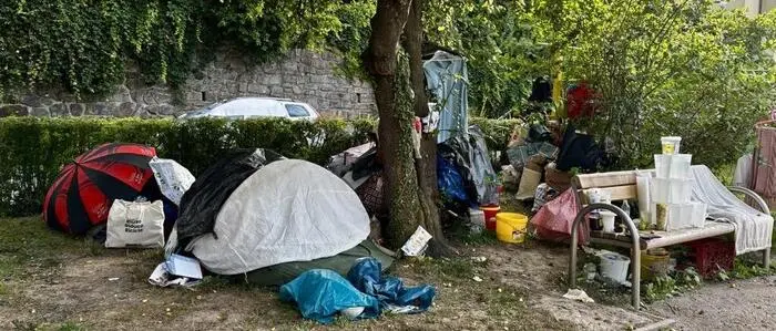 Eine Grünfläche auf der ein Zelt, Planen, Regenschirme und Hausrat stehen