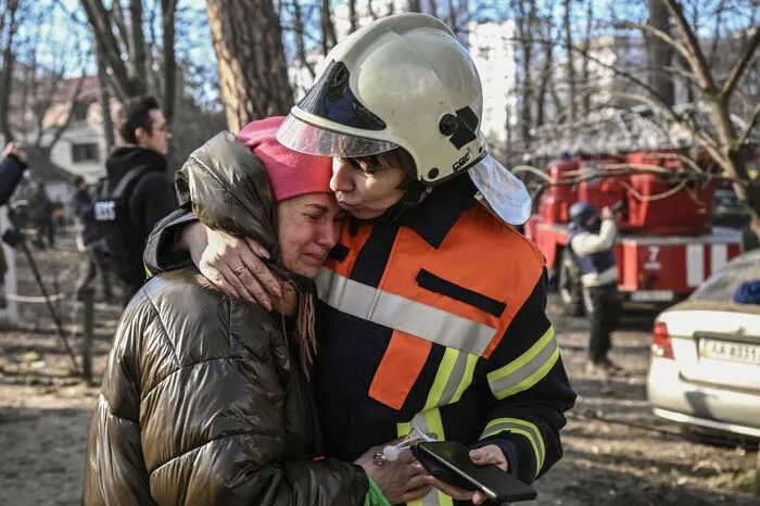 Eine  Feuerwehrfrau tröstet eine Bewohnerin nach einem Angriff in Kharkiv, bei dem ein Hochhaus zerstört wurde. 