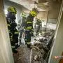 Man sieht Feuerwehrleute in einer vom Feuer stark in Mitleidenschaft gezogenen Wohnung | Das Feuer zerstörte einen Raum beinahe komplett