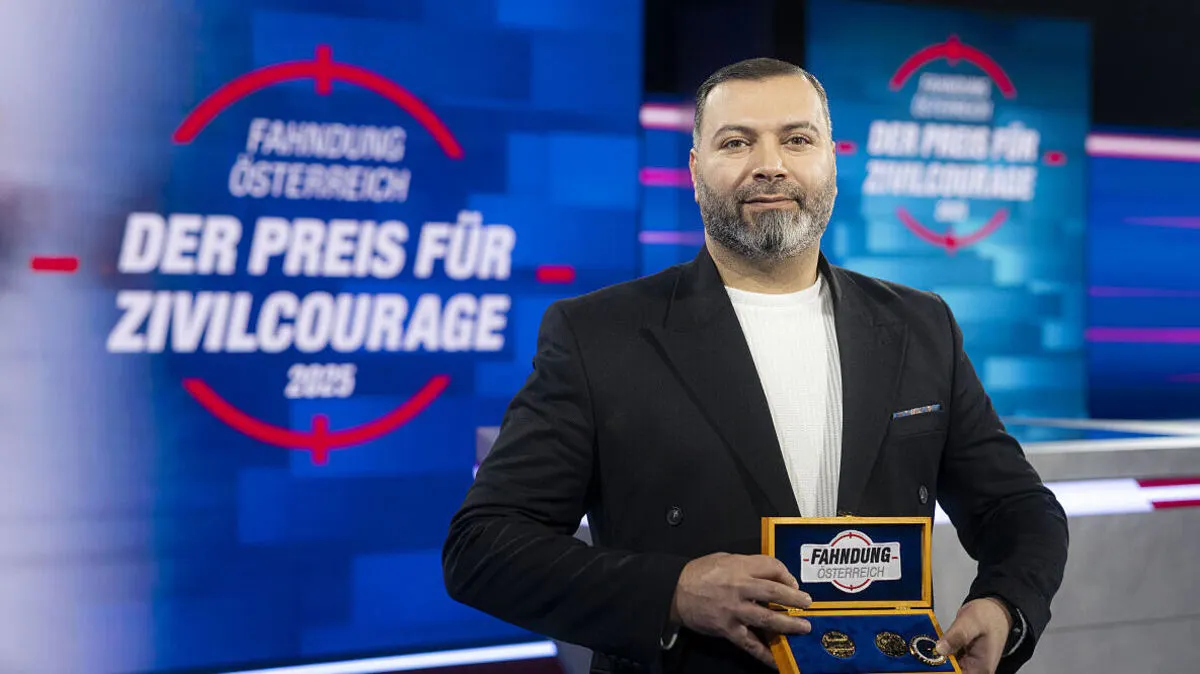 Man sieht einen Mann mit schwarzem Sakko vor einem Screen einen Preis in die Kamera haltend | „Fahndung Österreich - Preis für Zivilcourage“-Gewinner Allaaeddin Alhalabi