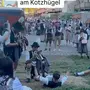 Eine große Menschenmenge beobachtet zwei Trompeter, die in Richtung eines Mannes spielen, der sich gerade aufrichtet. Darüber sieht man die Aufschrift „POV: Geweckt werden am Kotzhügel“. | „Is schon still uman See“ spielten die beiden Trompeter auf der Kotzwiese gegenüber des Festgeländes am Oktoberfest