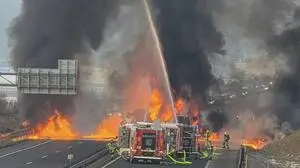 Man sieht Feuerwehrwagen auf einer Autobahn vor einem gewaltigen Feuer und dicken schwarzen Rauchsäulen | Das Feuer und die Rauchschwaden waren nach dem tödlichen Unfall weithin zu sehen