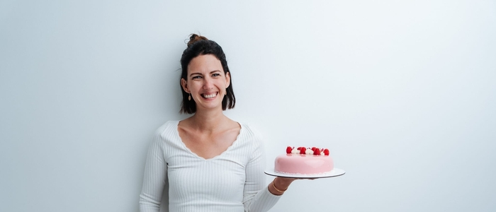 Man sieht eine Frau in die Kamera lachen, dabei hält sie eine Torte in der Hand