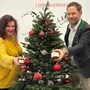 Eine Frau mit gelbem Oberteil und ein Mann in Sakko halten Honiggläser in die Kamera; in der Mitte sieht man einen geschmückten Christbaum | Erika Strieder und Arno Kronhofer vom Landesverband für Bienenzucht 