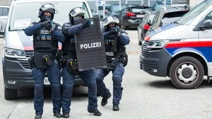 Drei Polizisten mit Schutzausrüstung vor zwei Einsatzwagen