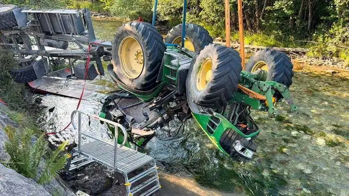 Man sieht einen ramponierten Traktor, der aus einem Bach gehoben wird