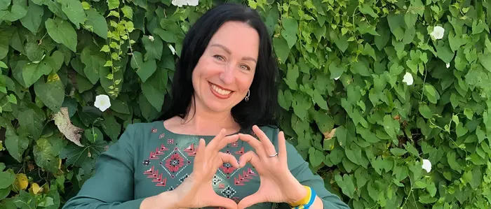 Frau mit schwarzen Haaren formt ein Herz mit ihren Händen und trägt traditionelle Kleidung aus der Ukraine