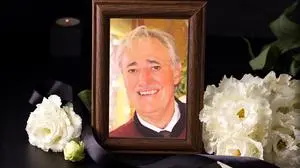 Ein Mann mit grauen Haaren lacht in die Kamera, sein Bild ist in einem braunen Bilderrahmen, um ihn herum sind weiße Blumen und eine schwarze Trauerschleife.  | Franz Käfer war bis zu seiner Pension Polizeiinspektionskommandant