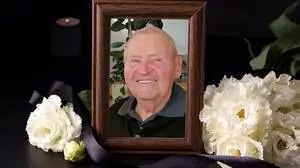 Ein Bilderrahmen mit Blumen an der Seite umrahmt einen Mann, der in die Kamera lacht