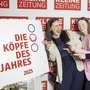 Drei junge Frauen zeigen lachend auf das „Köpfe des Jahres“-Schild