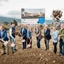 Mehrere Personen werfen beim Spatenstich mit einer Schaufel Erde in die Luft