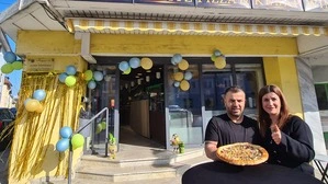 Ein Paar hält eine Pizza in die Kamera, im Hintergrund steht „Blitz Pizza & Kebap“ am Schild über dem Eingang 