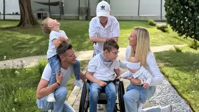 Vier Kinder mit ihren Eltern, eines davon sitzt im Rollstuhl und alle tragen Jeans mit einem weißen Oberteil