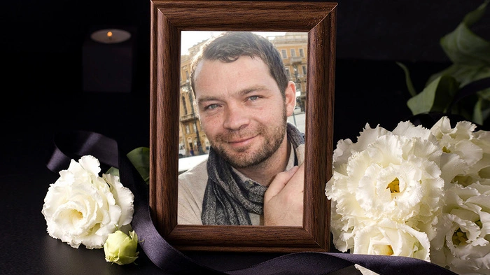Der Verstorbene ist in einem Bilderrahmen zu sehen, nebenan liegen weiße Blumen
