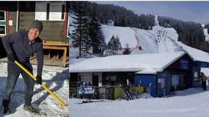 Ein Mann mit einer Schneeschaufel und eine verschneite Almhütte
