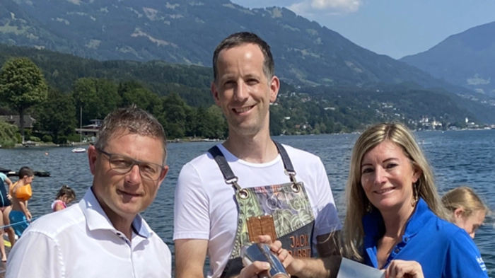 Drei Menschen mit einem Plakat auf einem Steg vor einem See