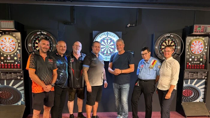Sieben Personen stehen in einer Dart-Halle