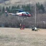 Zwei Männer hängen etwas an einen Hubschrauber, der in wenigen Metern über dem Boden schwebt