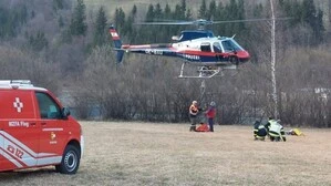 Zwei Männer hängen etwas an einen Hubschrauber, der in wenigen Metern über dem Boden schwebt
