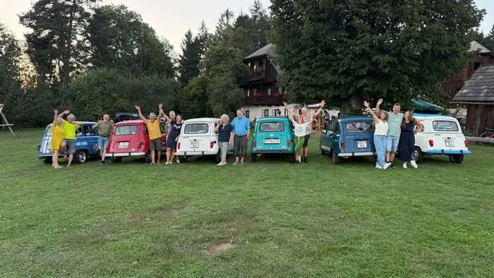 Menschen stehen mit ihren Autos auf einer Wiese