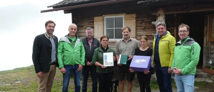 Mehrere Personen stehen mit Urkunden vor einer Almhütte