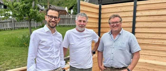 Drei Männer stehen vor einer Holzwand