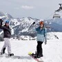 Zwei Snowboarderinnen stehen auf einer verschneiten Piste und winken