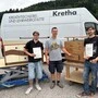 Drei Männer stehen vor Werkstücken aus Holz und einem Fahrzeug
