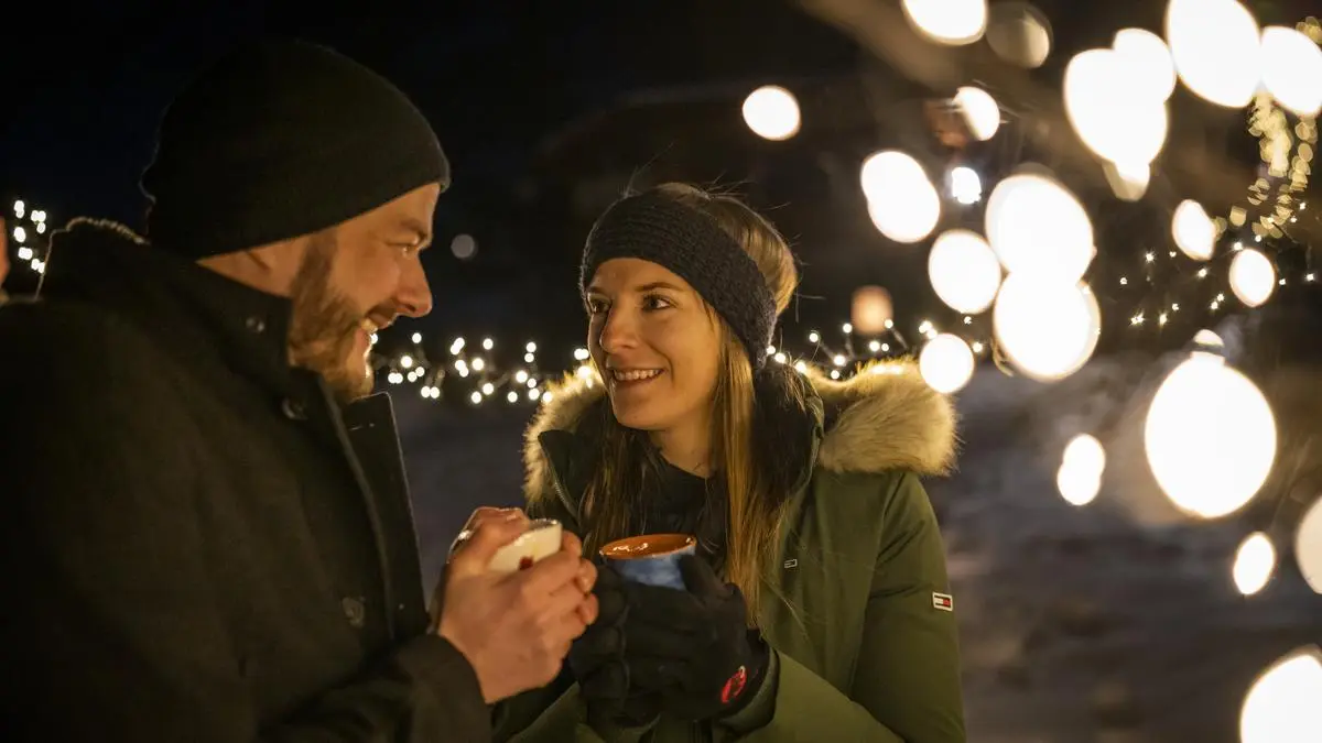 Ein Mann und eine Frau stehen im Winter auf einem mit Schnee bedeckten Feld und schauen sich verliebt an | In Mittelkärnten gibt es verschiedene Angebote, um den Jahresausklang zu feiern