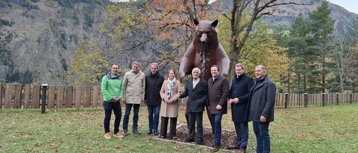Mehrere Personen stehen vor einer Bären-Statue in einem Park